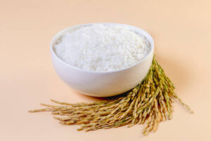 cooked rice in a bowl and ears of rice on a pink background
